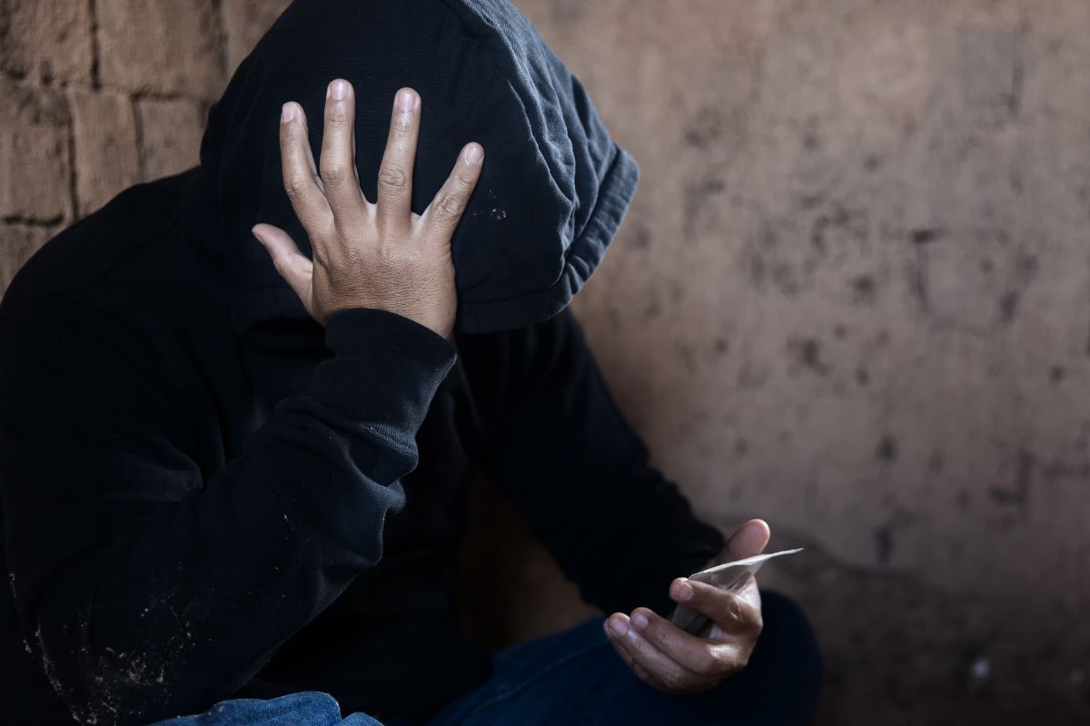 Person in a hoodie holding a small packet. Person in a hoodie holding a small packet.