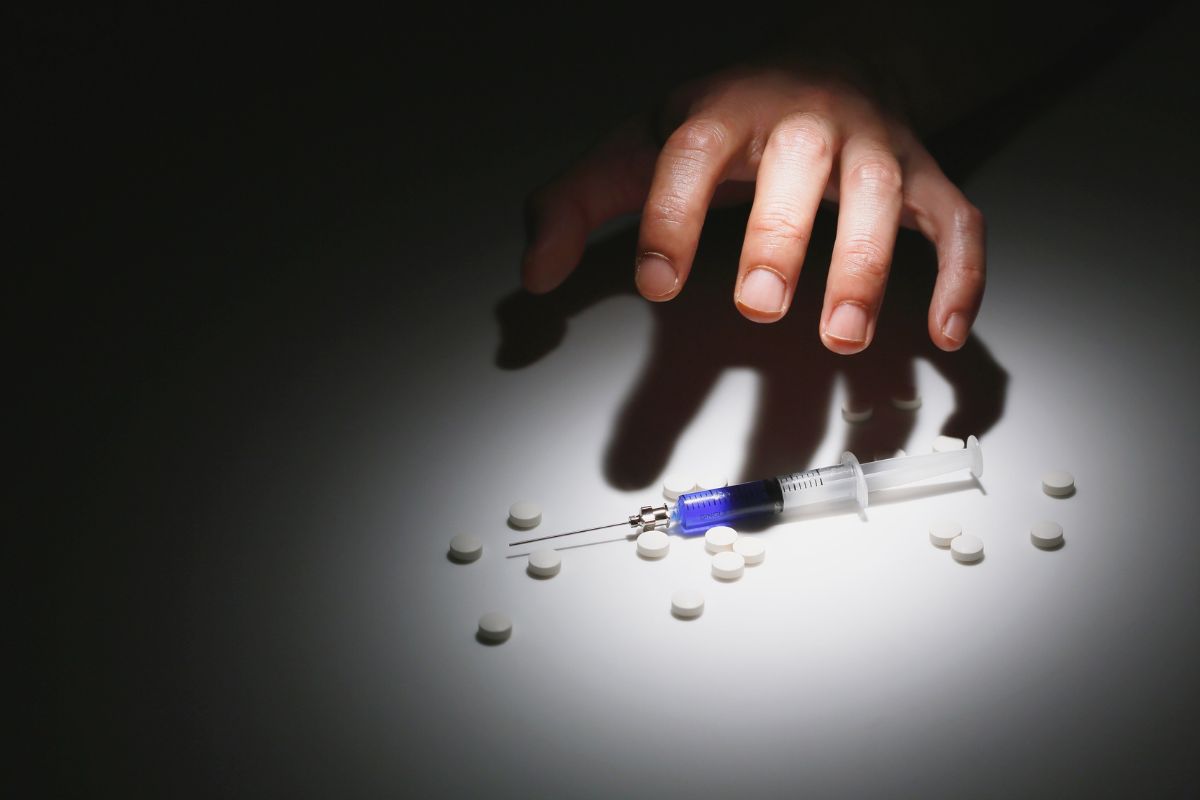 Hand reaching toward a syringe and pills. Hand reaching toward a syringe and pills.