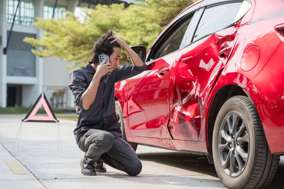 Man calling for help while inspecting damage on a red car after an accident. Man calling for help while inspecting damage on a red car after an accident.