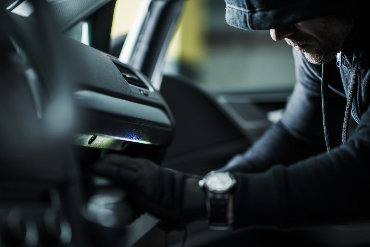 Hooded person searching a car’s glove box. Hooded person searching a car’s glove box.