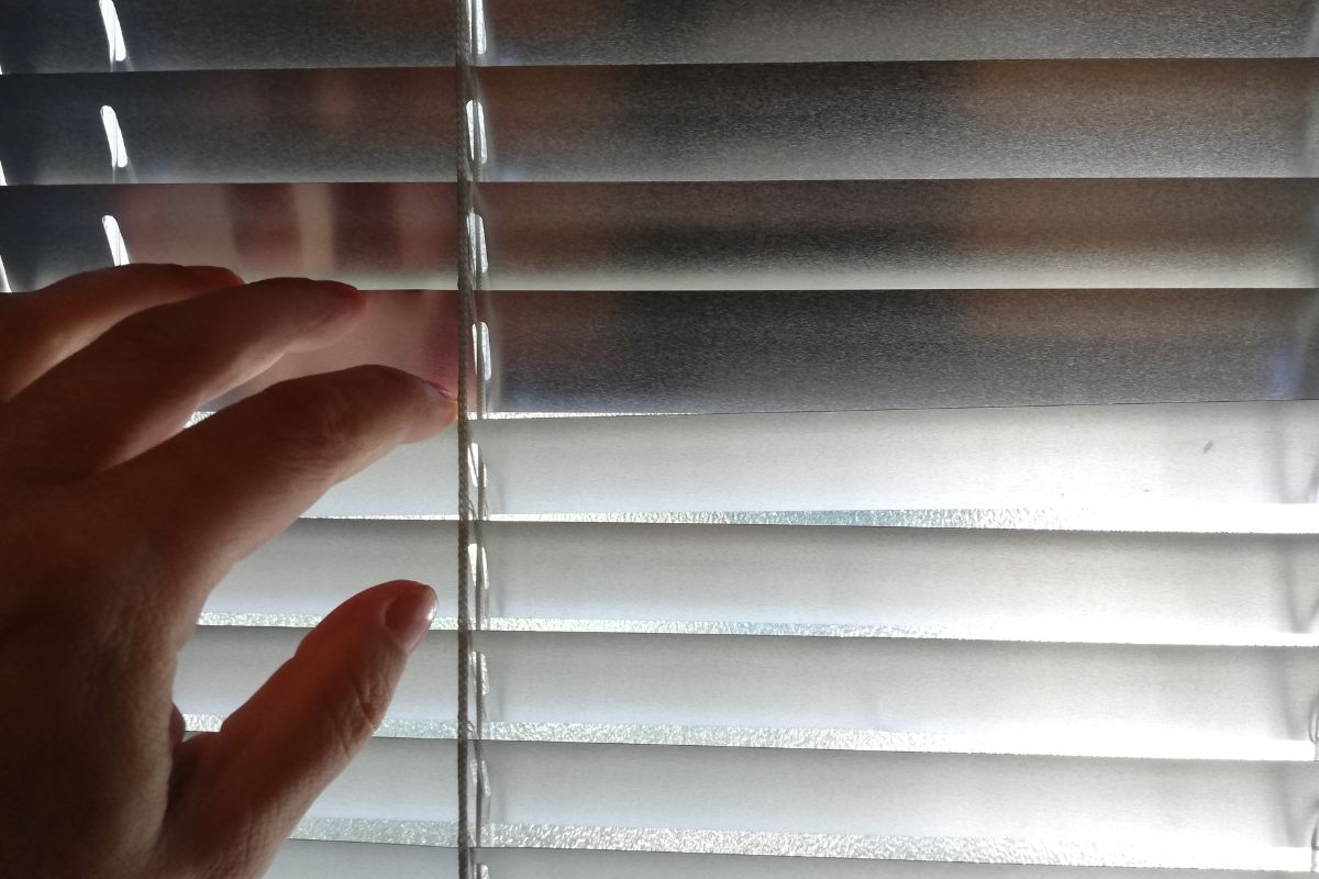 Hand opening window blinds to look outside. Hand opening window blinds to look outside.