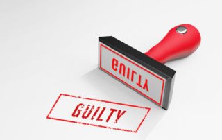 Red rubber stamp marking the word “GUILTY” on paper.