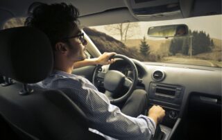 Man driving a car on a winding rural road.