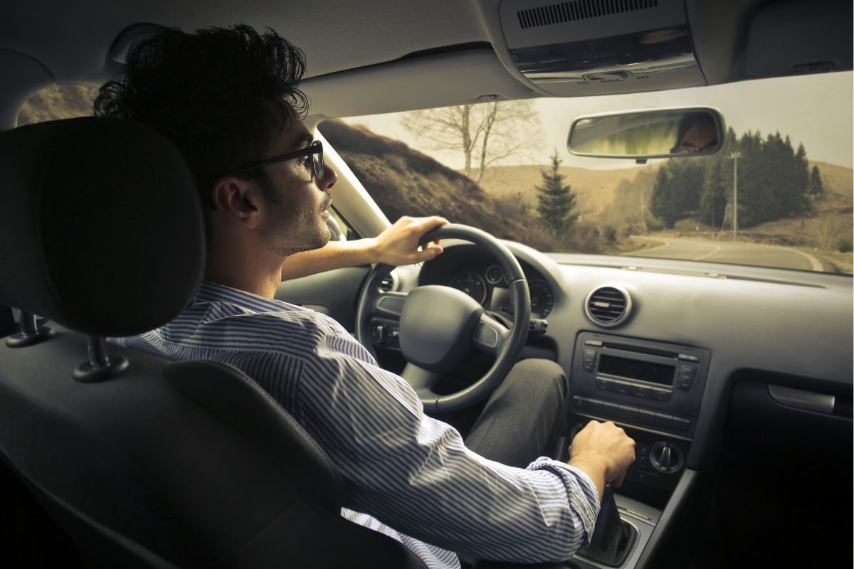 Man driving a car on a winding rural road.