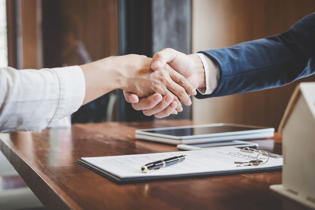 Two people shaking hands over legal documents.