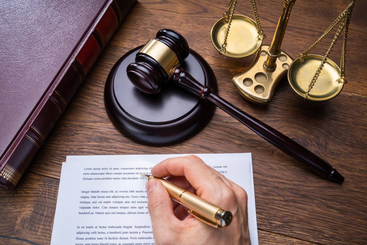 A judge writing on a legal document with a gavel, scales of justice, and a law book.