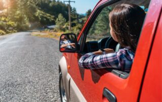 A woman is driving a red car on a rural road.
