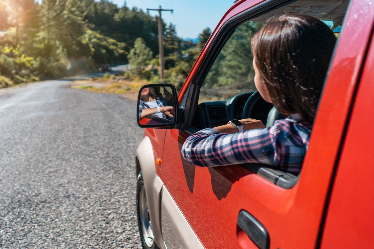 A woman is driving a red car on a rural road.
