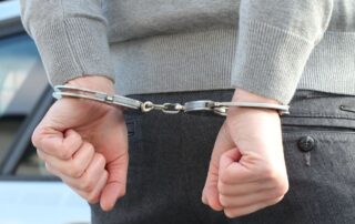 Arrested man in handcuffs behind back representing criminal charges and warrant.