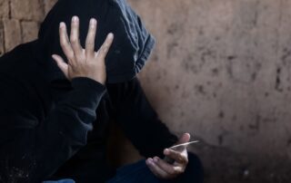 A man is covering their face while holding a small packet of drugs.