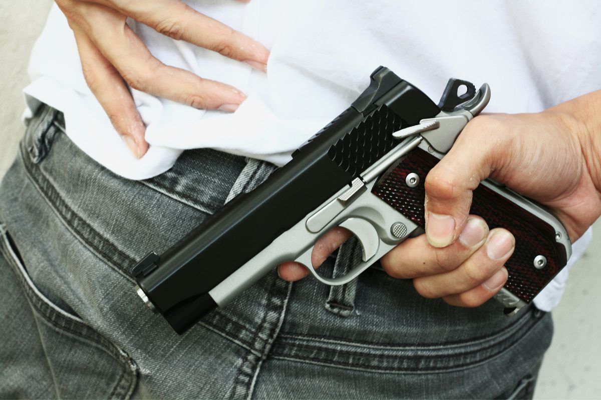 A man holding a handgun tucked into his waistband.