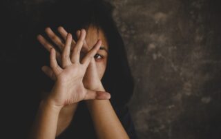 A woman with a bruised face holds her hands up in fear.