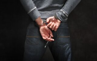 A man in handcuffs holding a syringe behind their back.