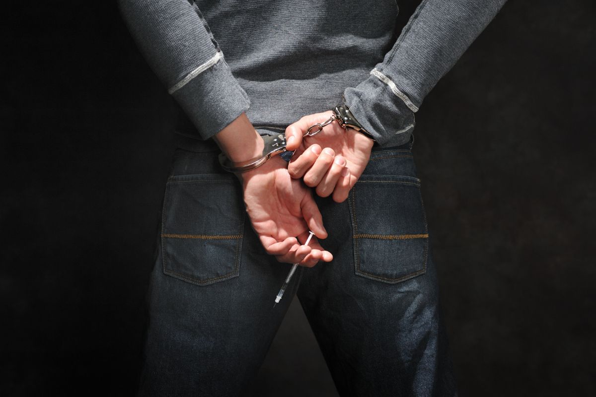 A man in handcuffs holding a syringe behind their back.