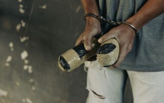 A man in handcuffs holding two taped packages.