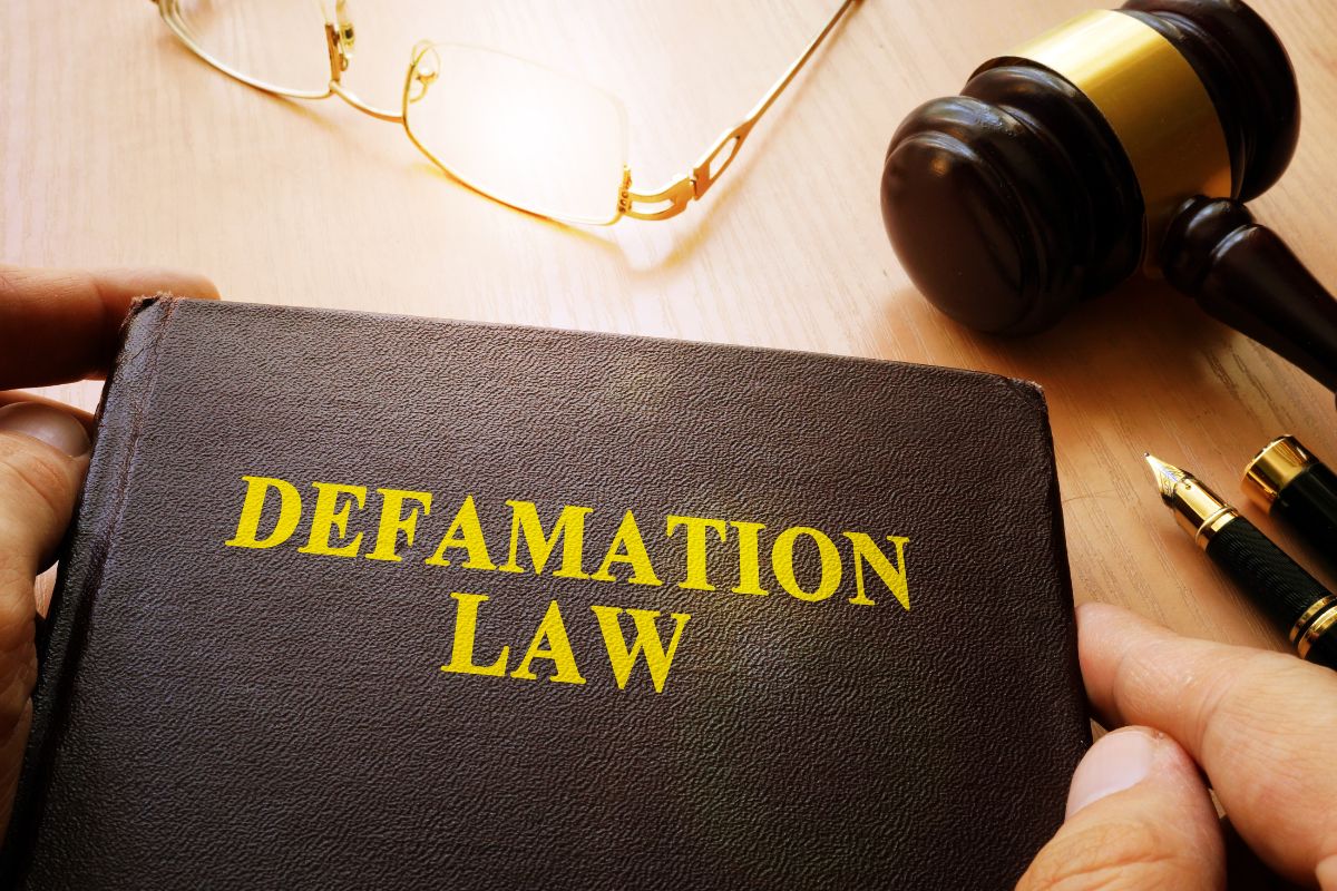 Person holding a book titled "Defamation Law" with a gavel, glasses, and pen.
