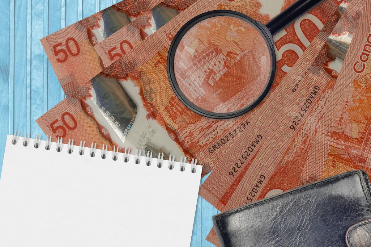 Canadian $50 bills under a magnifying glass, with a wallet and notepad