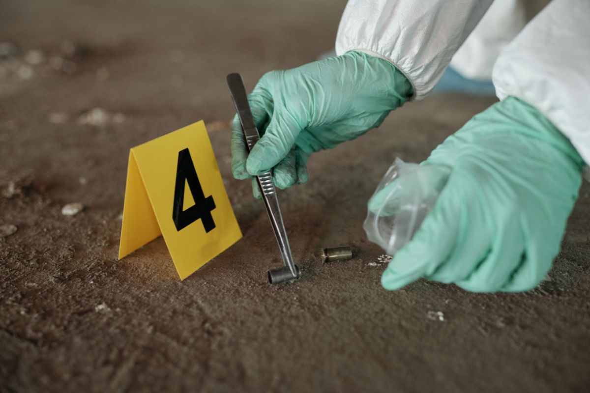 Investigator collecting bullet casing evidence at a crime scene.