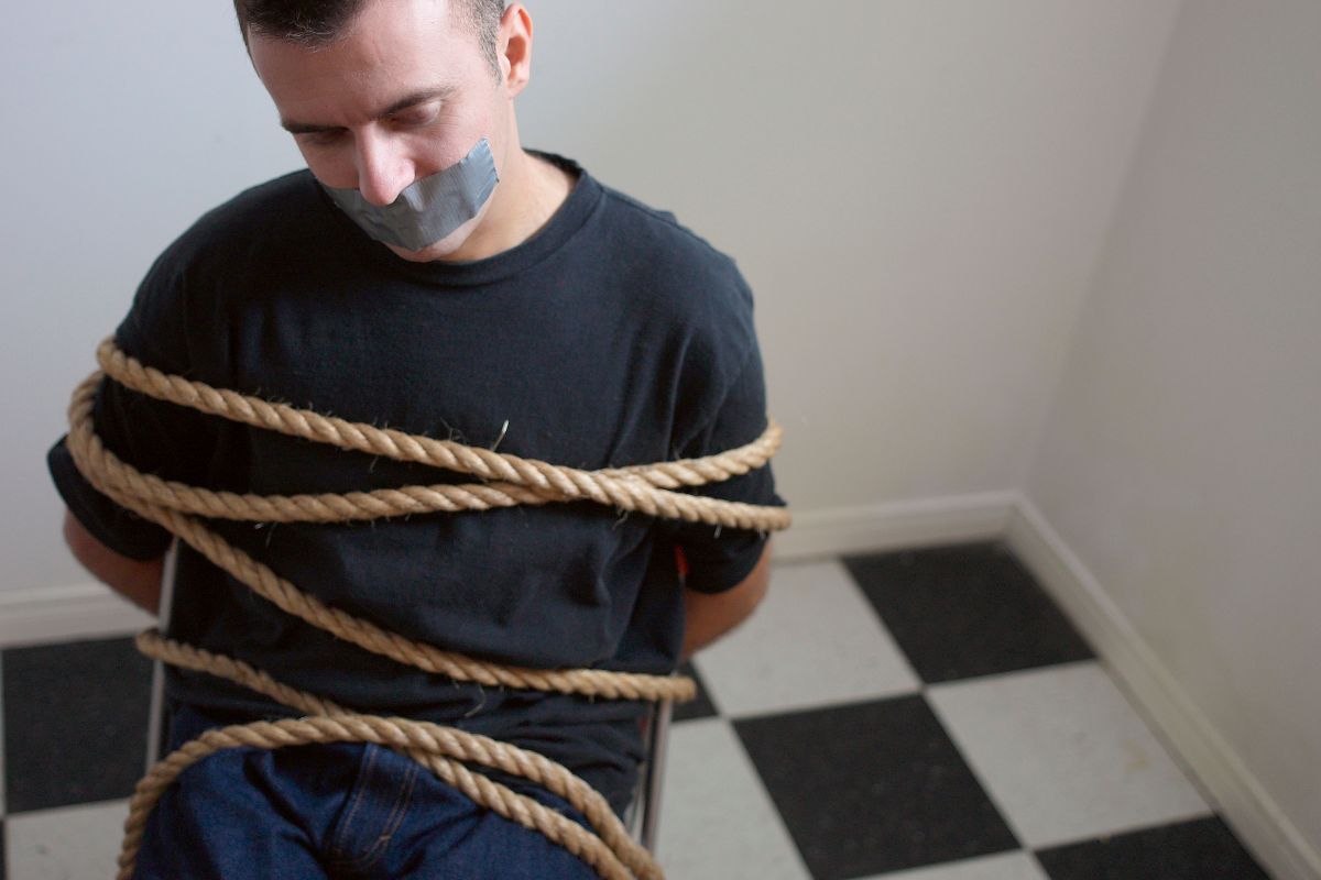 A man tied to a chair with rope and duct tape over his mouth.