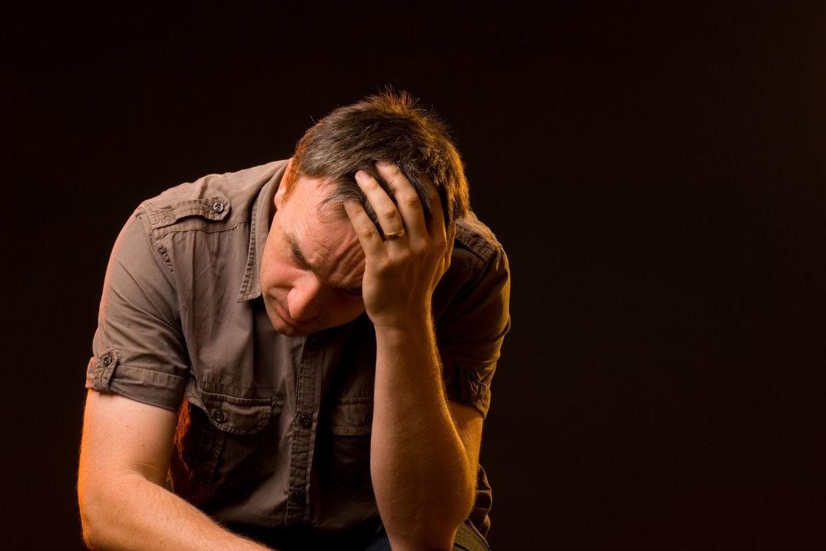 A distressed man sitting with his head in his hand.