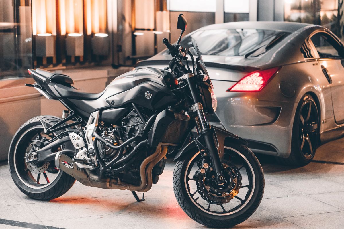 Black motorcycle and silver sports car parked.