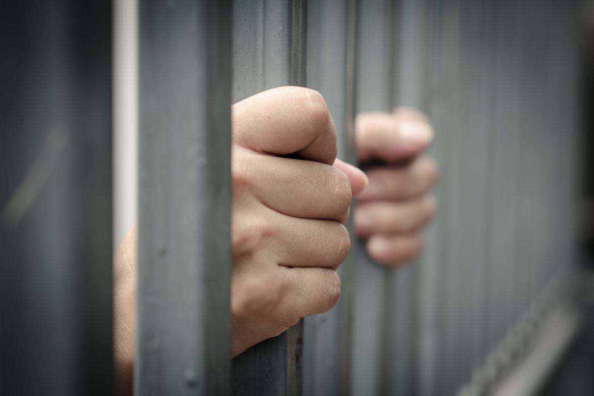 Close-up of hands gripping jail bars.