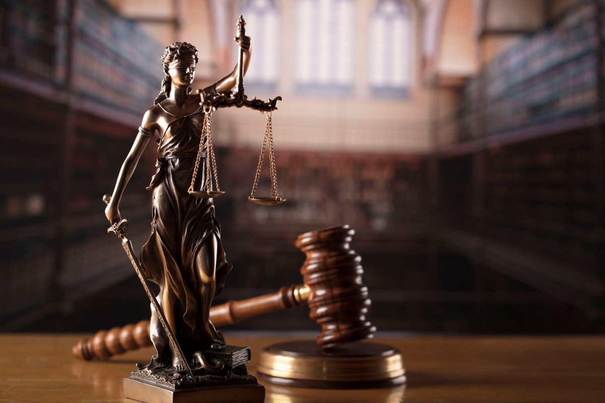 Statue of Lady Justice with scales and a gavel in a courtroom.