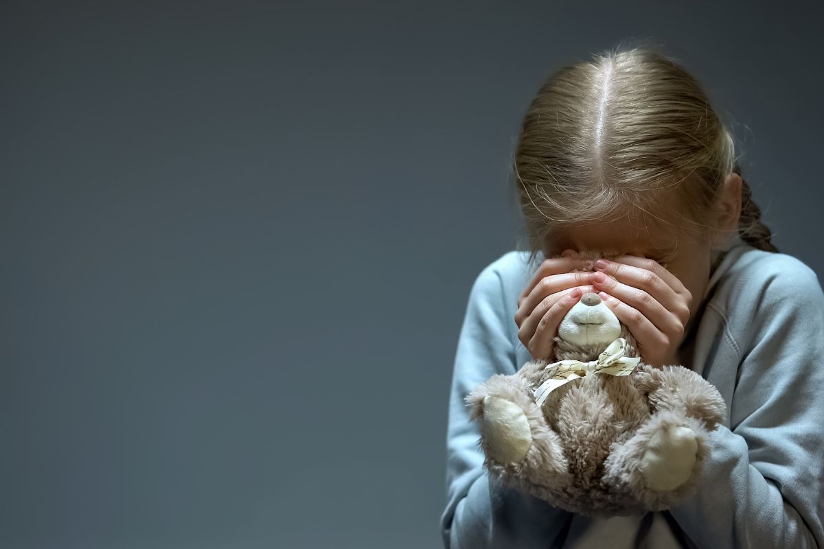 A young girl holding a teddy bear covering her face.