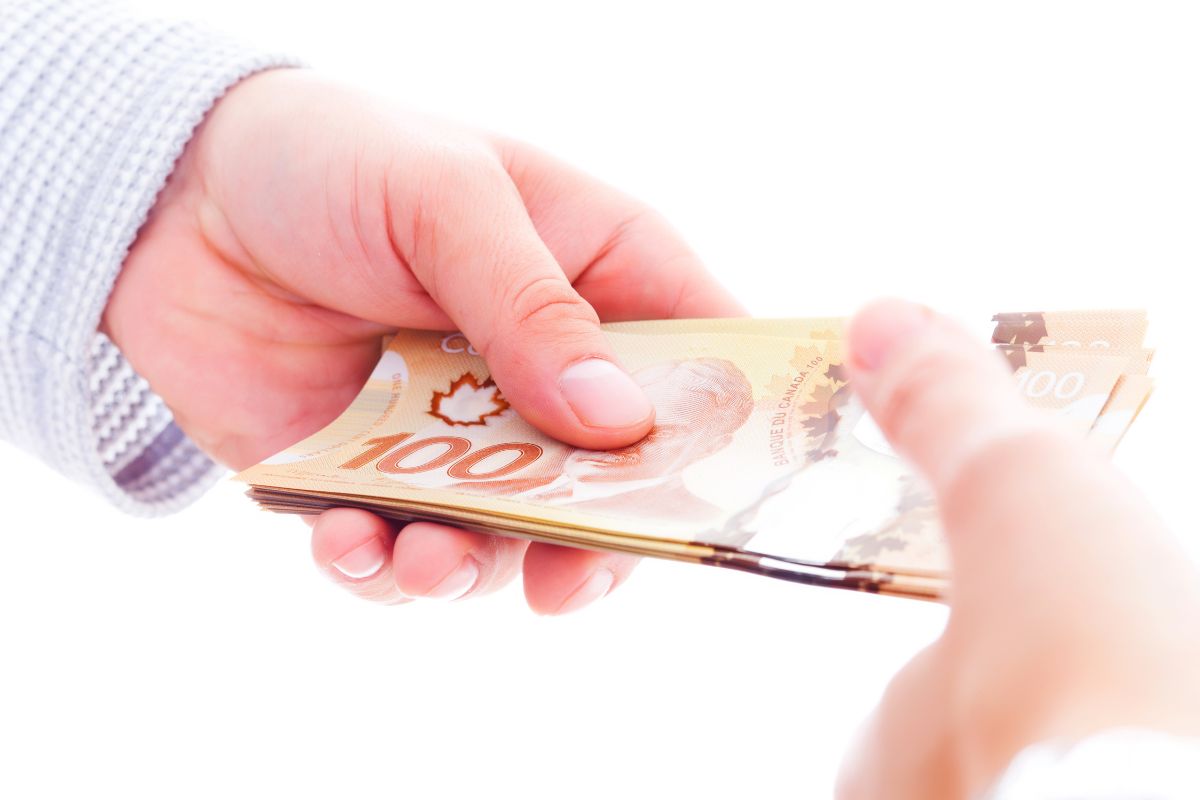 Close-up of hands exchanging Canadian $100 bills.