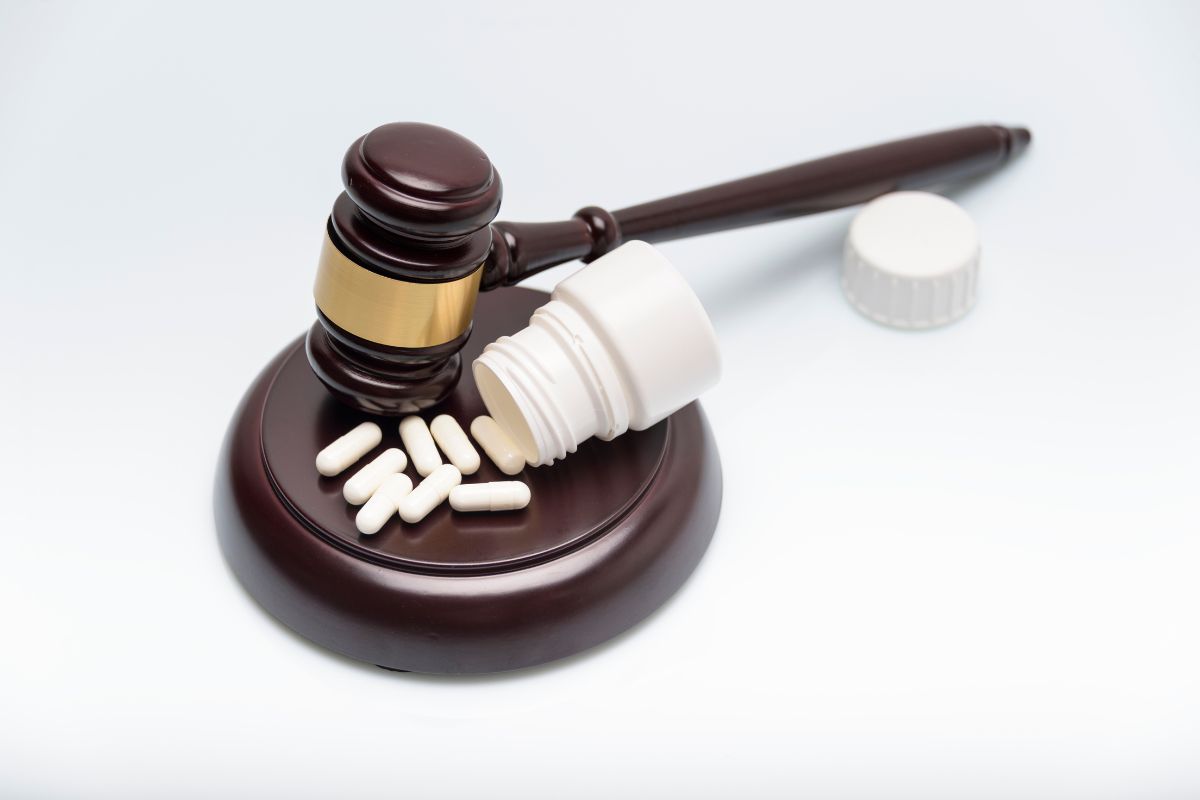 Judge’s gavel next to an open pill bottle and scattered capsules,