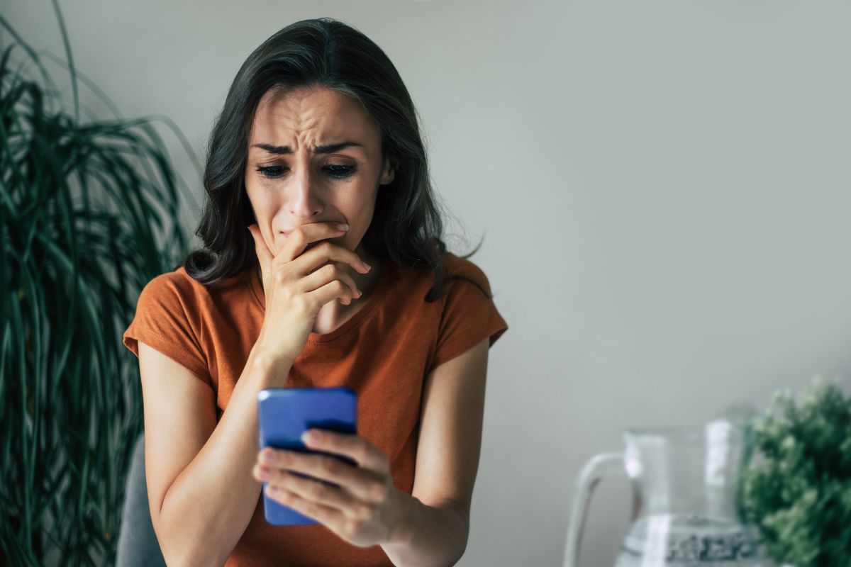 A sad woman is crying while looking at her phone.