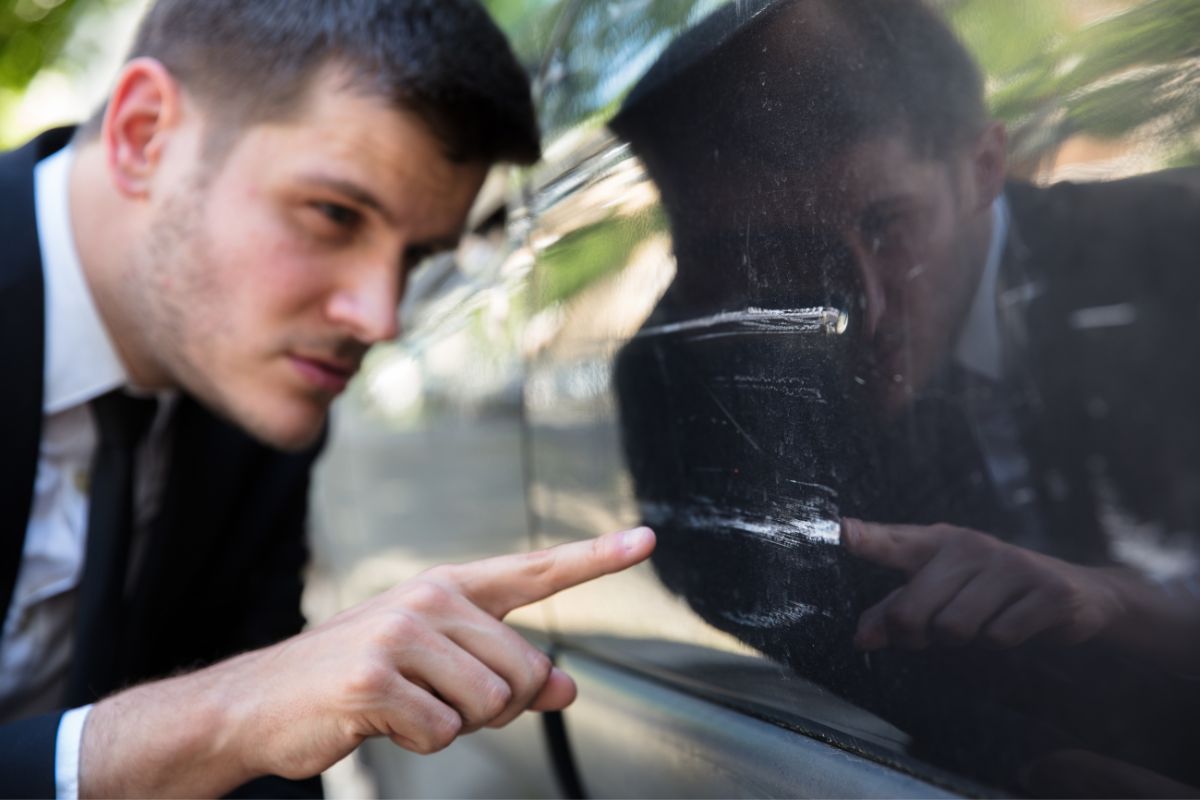 Man inspecting a scratch on a car door.