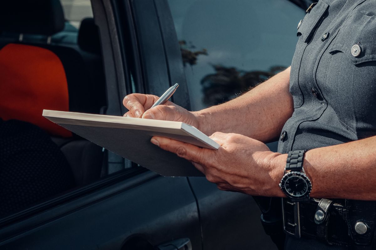 A police officer writing on a notepad beside a vehicle.