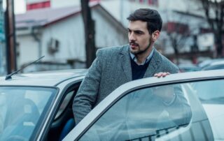 A man in a coat entering a car.