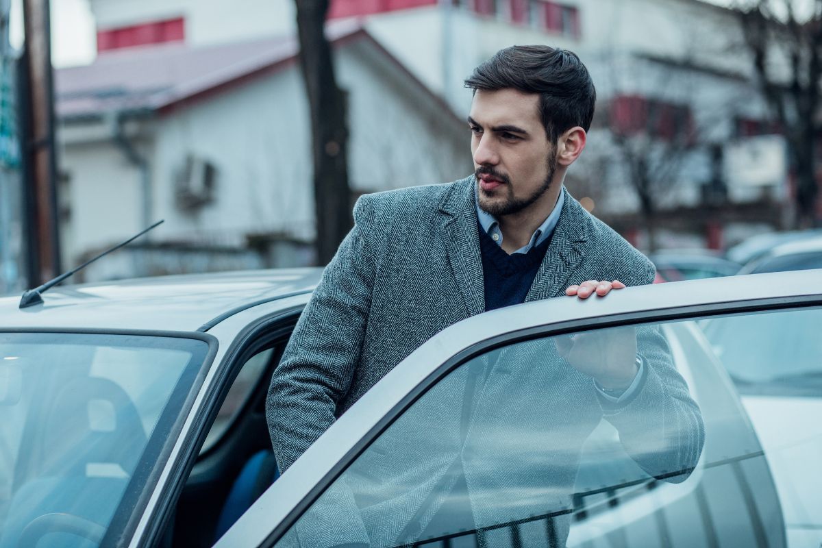 A man in a coat entering a car.