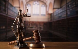 Lady Justice statue with scales and a gavel in a courtroom.