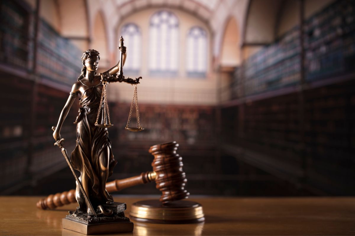Lady Justice statue with scales and a gavel in a courtroom.