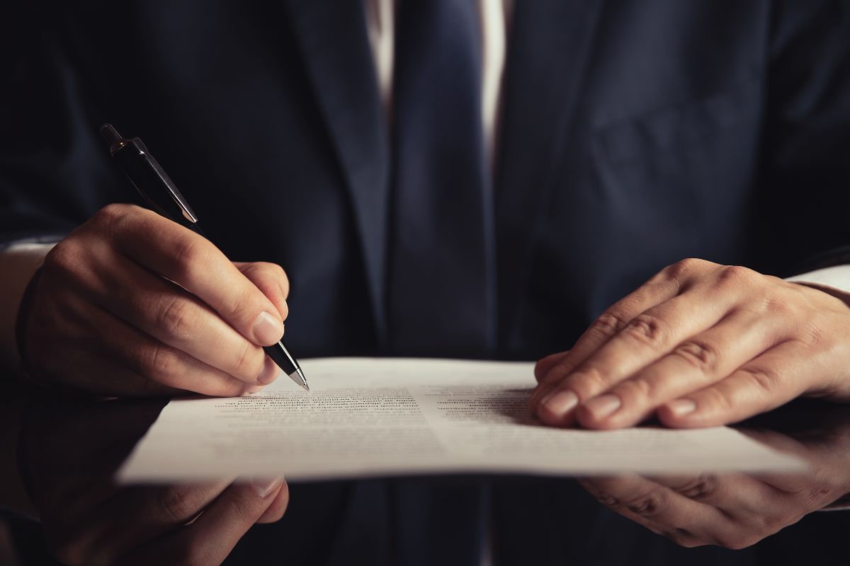 A lawyer in a suit signing legal documents on a desk.