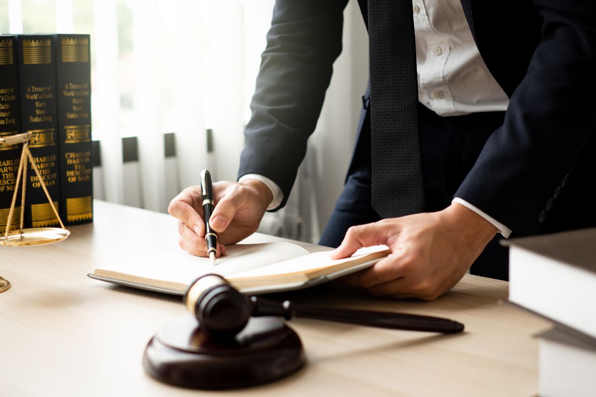 A lawyer writing in a legal book at a desk with a gavel and scales of justice. A lawyer writing in a legal book at a desk with a gavel and scales of justice.
