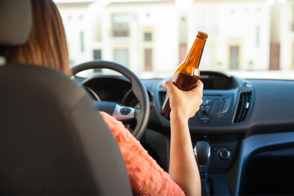 A driver holding a beer bottle inside a car. A driver holding a beer bottle inside a car.
