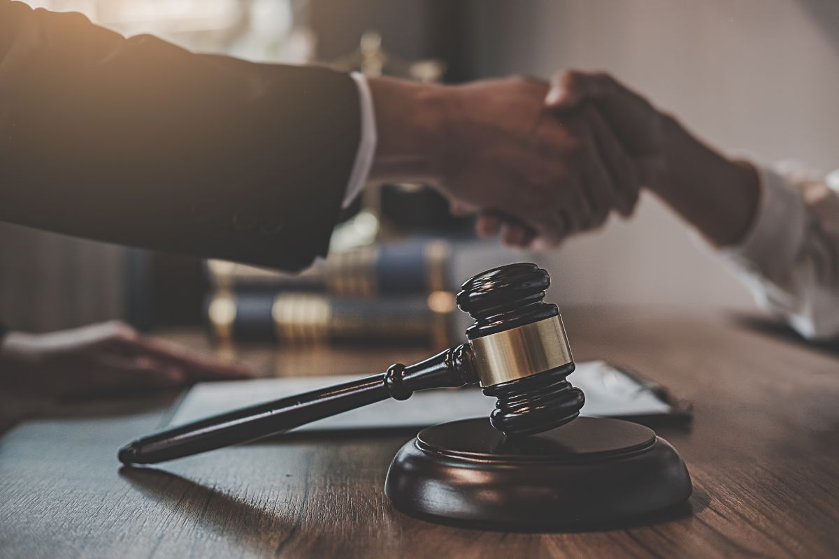 A gavel on a desk with two people shaking hands.