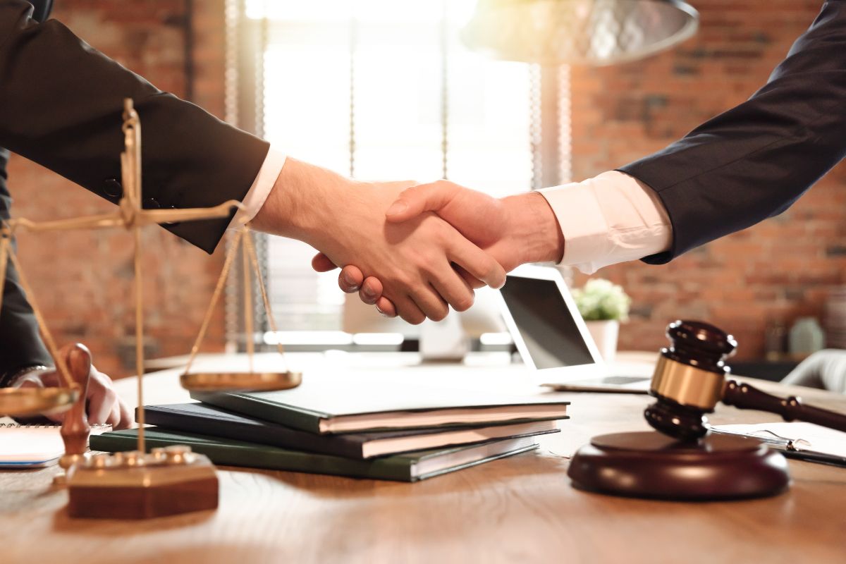 Handshake at a lawyer’s desk with documents, scales, and a gavel. Handshake at a lawyer’s desk with documents, scales, and a gavel.
