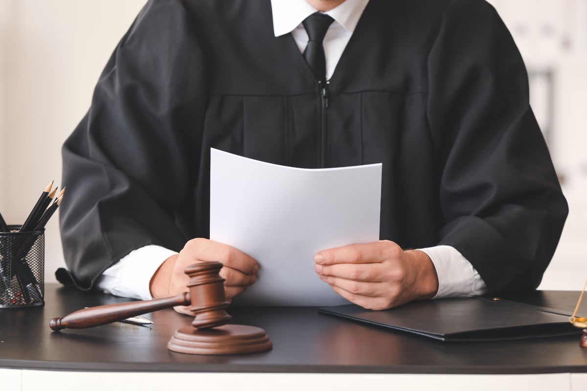 A judge holding a document at a desk with a gavel and legal stationery. A judge holding a document at a desk with a gavel and legal stationery.