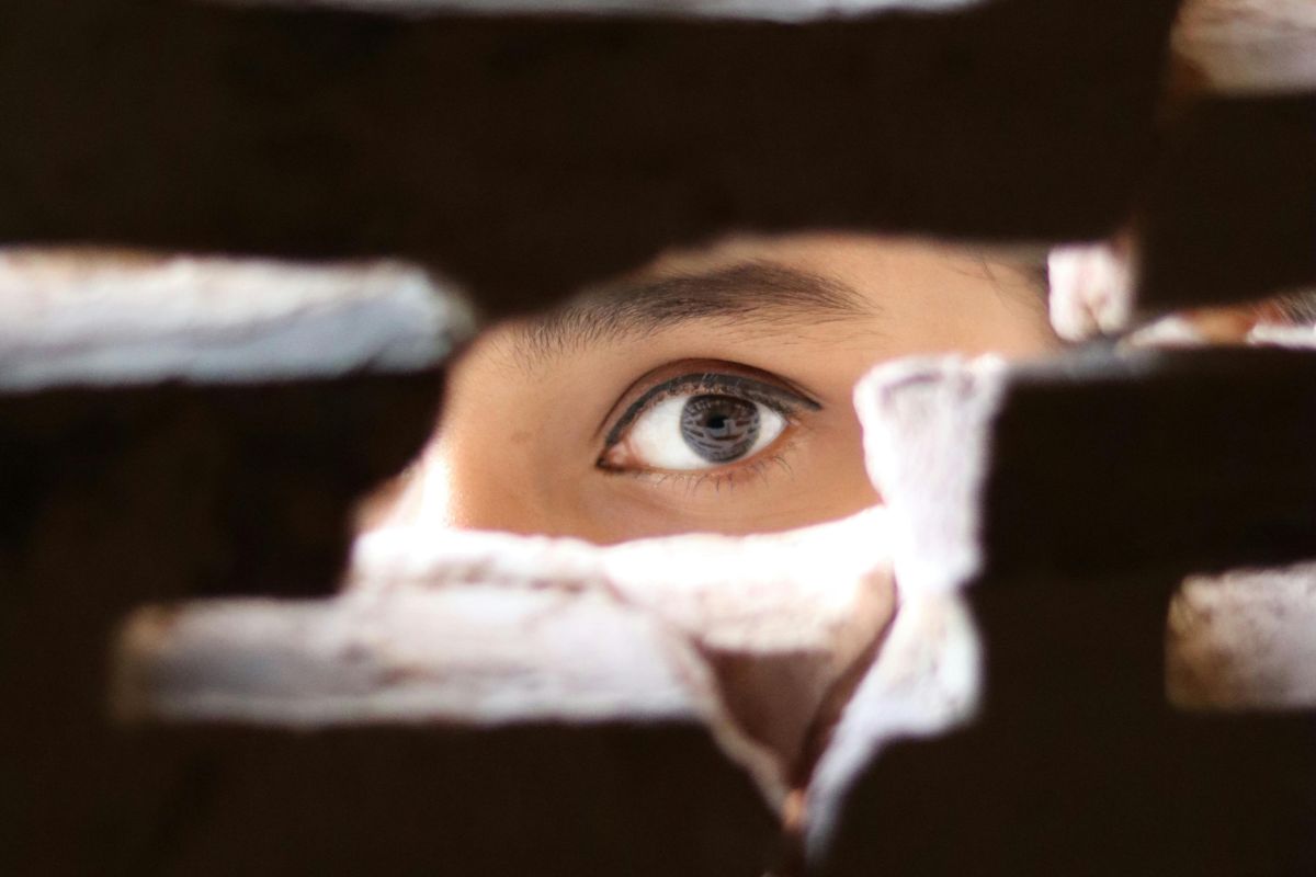 An eye peering through a small gap in a wall. An eye peering through a small gap in a wall.