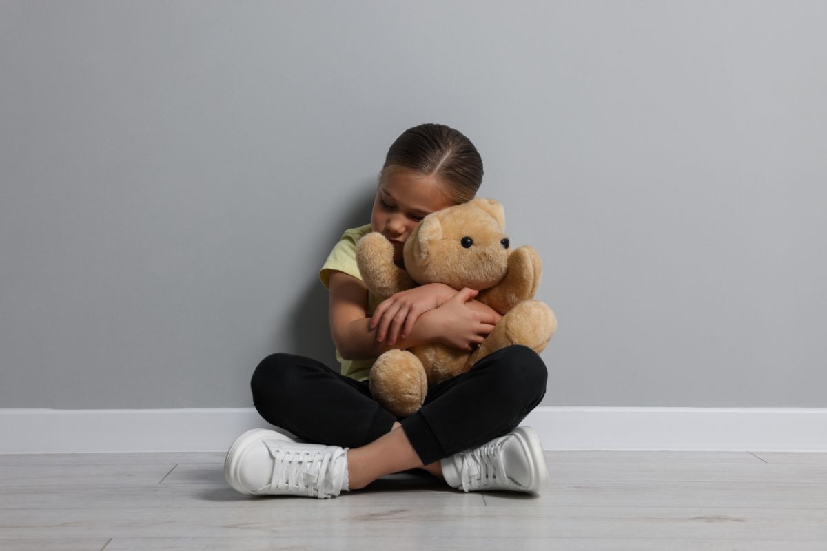 Sad child sitting on the floor holding a teddy bear. Sad child sitting on the floor holding a teddy bear.