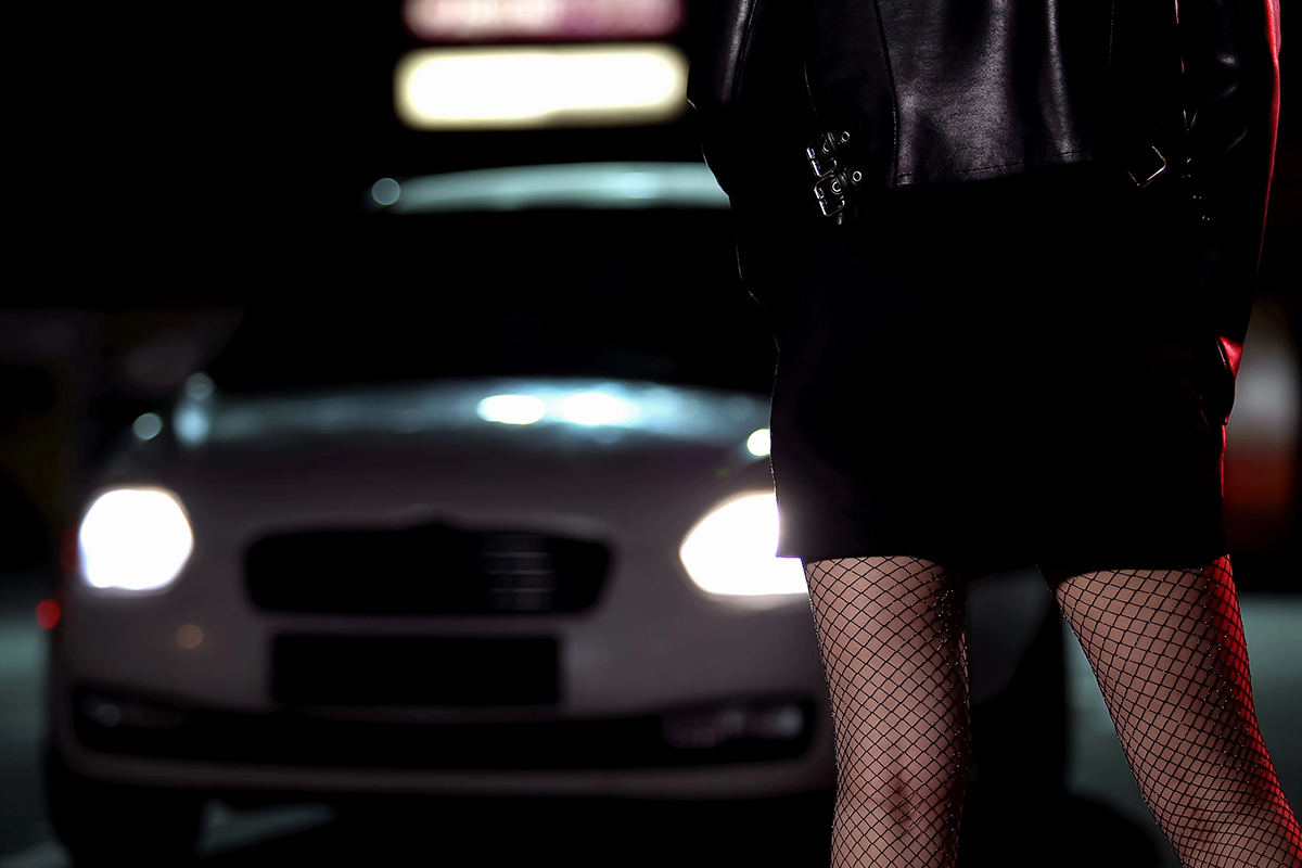 A sex worker stands in front of a vehicle