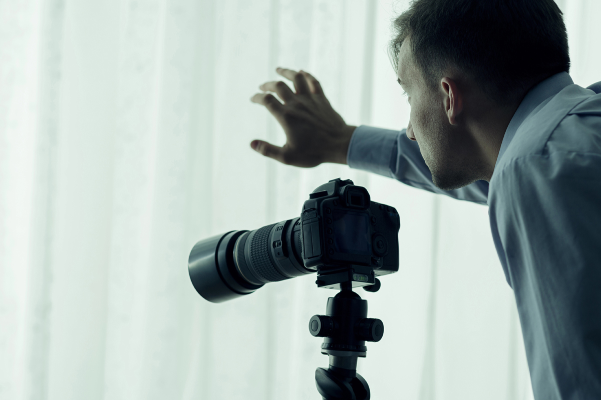 A man stands at a window with a camera.