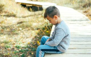A young boy sitting alone on a wooden path.