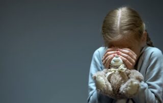 A young girl holding a teddy bear covering her face.
