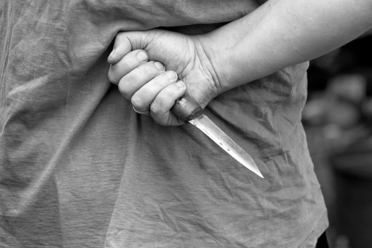 A person holding a knife behind their back. A person holding a knife behind their back.